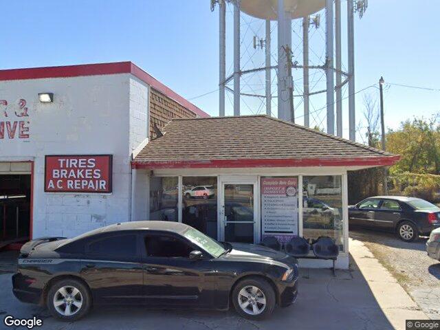 The J and M Tire and Muffler shopfront on South Hall Street: a white building with red trim, a sign reading tires, brakes, A C repair, and the Webb City water tower behind it